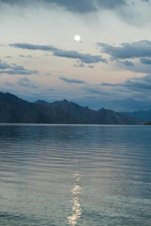 a large body of water with mountains in the background, by Muggur, with the moon out, day setting, boka, slight smirk