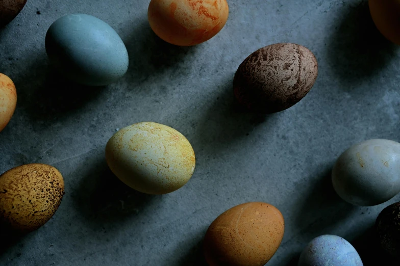 a table topped with lots of different colored eggs, by Jessie Algie, trending on unsplash, renaissance, dark grey and orange colours, slate, battered, close-up product photo