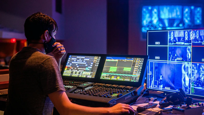 a man that is sitting in front of a computer, interactive art, softly glowing control panels, theatre equipment, avatar image, cinematic colour grading