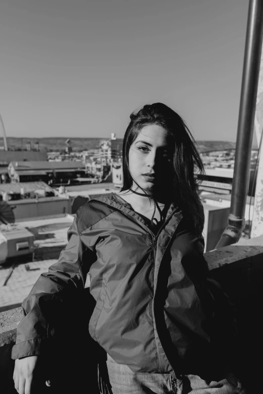 a black and white photo of a woman on a balcony, by Alexis Grimou, black haired girl wearing hoodie, she wears a jacket, ava max, on rooftop