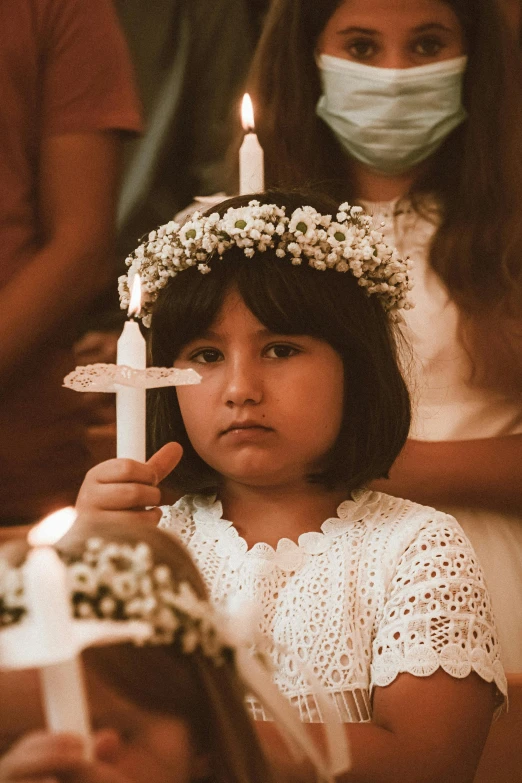 a little girl wearing a crown and holding a candle, a colorized photo, pexels contest winner, symbolism, holy ceremony, sad expression, white candles, npc with a saint's halo