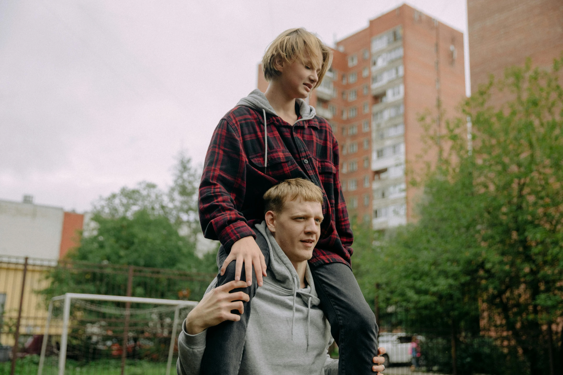 a man riding on the back of a woman on a skateboard, by Attila Meszlenyi, pexels contest winner, realism, blond boy, still image from tv series, two men hugging, in russia