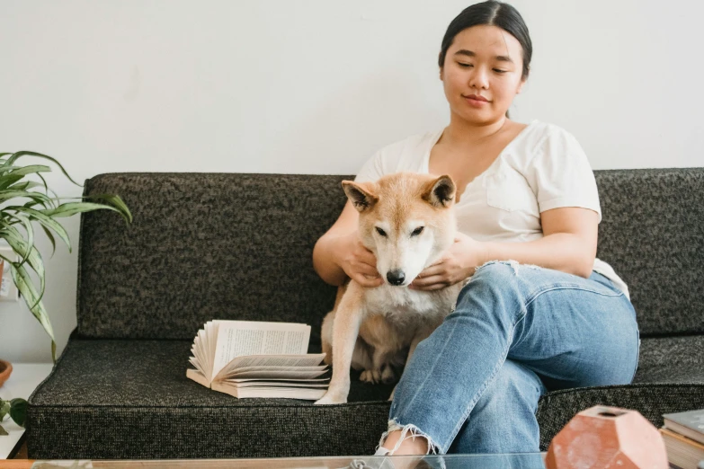 a woman sitting on a couch with a dog, trending on pexels, visual art, shiba inu, holding books, background image, asian descent