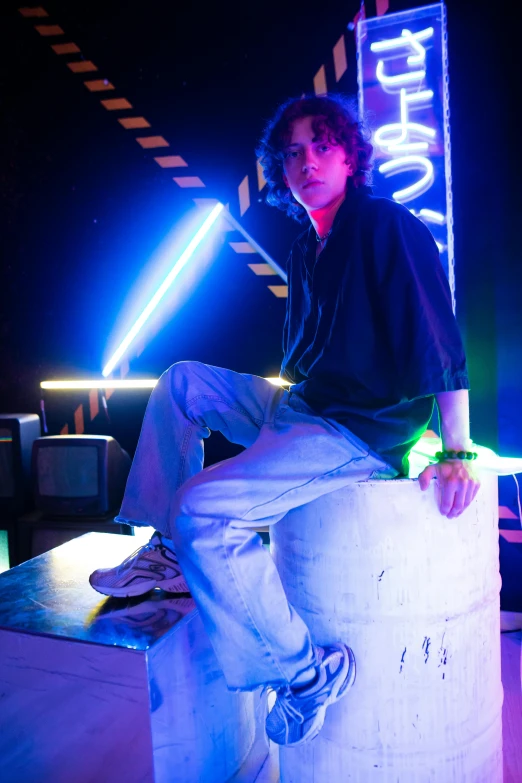 a man sitting on a block in front of a neon sign, happening, finn wolfhard, advanced stage lighting, with a cool pose, in a nightclub