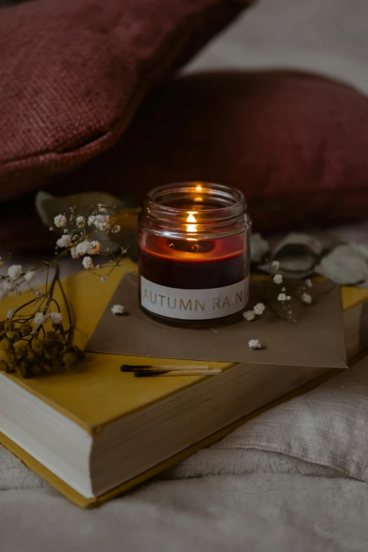 a candle sitting on top of a book on a bed, autumnal empress, radiant aura, crimson themed, glowing jar