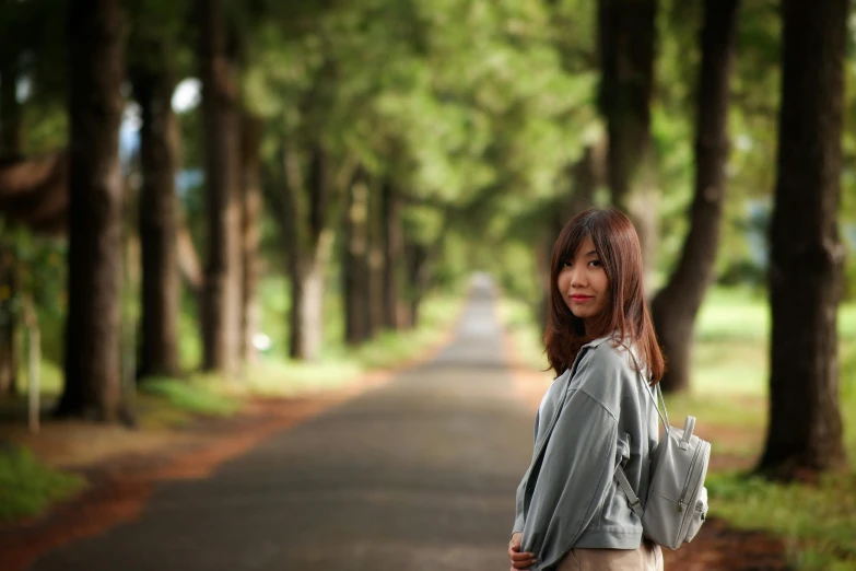 a woman standing in the middle of a road, a picture, inspired by Ma Yuanyu, pexels contest winner, realism, trees in the background, schools, shy smile, background image