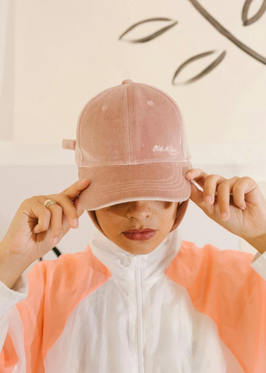 a woman putting a hat on top of her head, by Dulah Marie Evans, featured on instagram, faded pink, embroidered velvet, sleek visor, mai anh tran