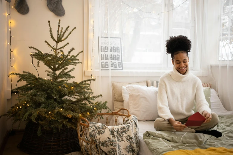 a woman sitting on a bed reading a book, pexels contest winner, happening, christmas tree, african american young woman, working on her laptop, a still of a happy