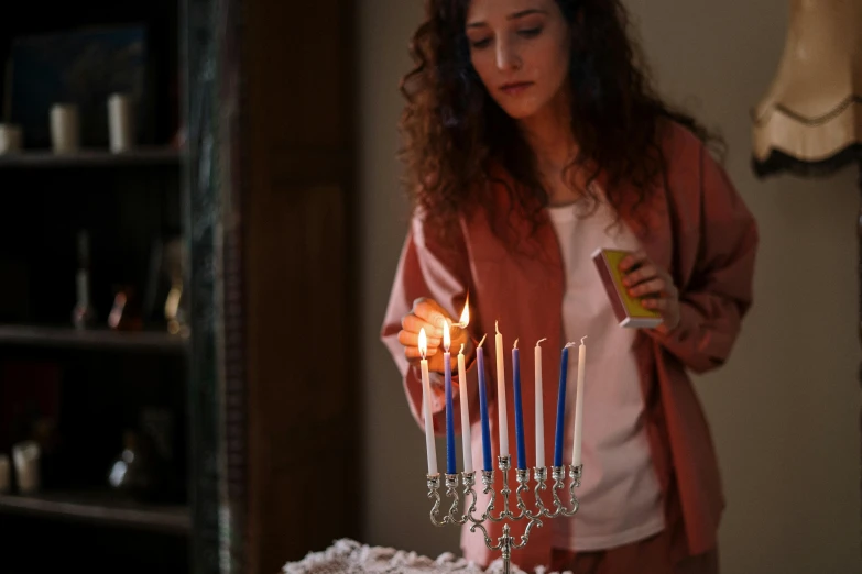 a woman blowing out candles on a cake, by Julia Pishtar, pexels, beautiful jewish woman, blue and silver colors, on a candle holder, walking down