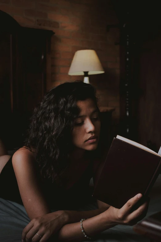 a woman laying in bed reading a book, a portrait, inspired by Elsa Bleda, pexels contest winner, standing in a dimly lit room, gif, light skin, with a black background