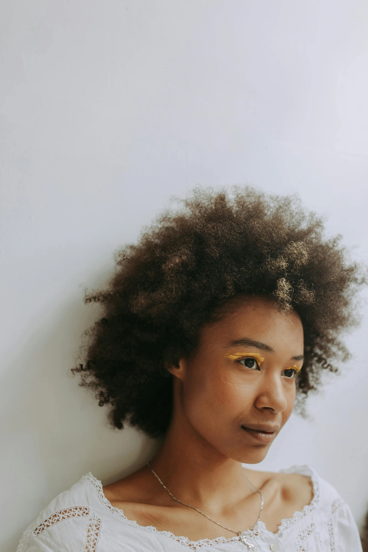 a woman standing in front of a white wall, trending on pexels, afrofuturism, wavy hair yellow theme, ( brown skin ), high angle closeup portrait, bedhead