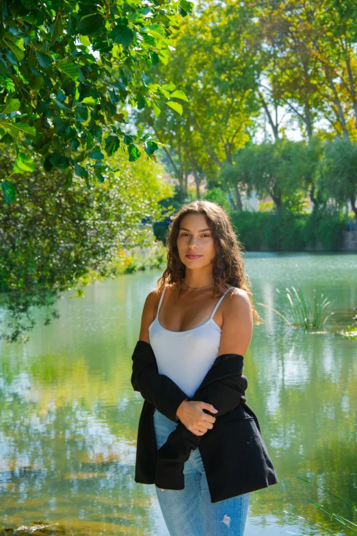 a woman standing next to a body of water, lush surroundings, seville, portrait demi rose, college