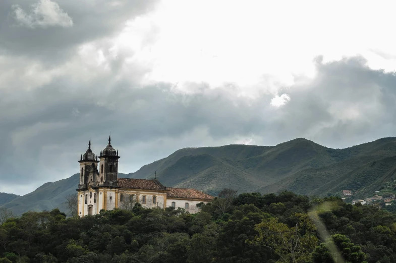 a church sitting on top of a lush green hillside, by Ceferí Olivé, baroque, fan favorite, brazil, grey skies, preserved historical