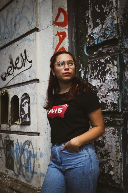 a woman standing in front of a wall with graffiti on it, an album cover, inspired by Elsa Bleda, pexels contest winner, wearing a black t-shirt, alexandria ocasio-cortez, reds), ((portrait))