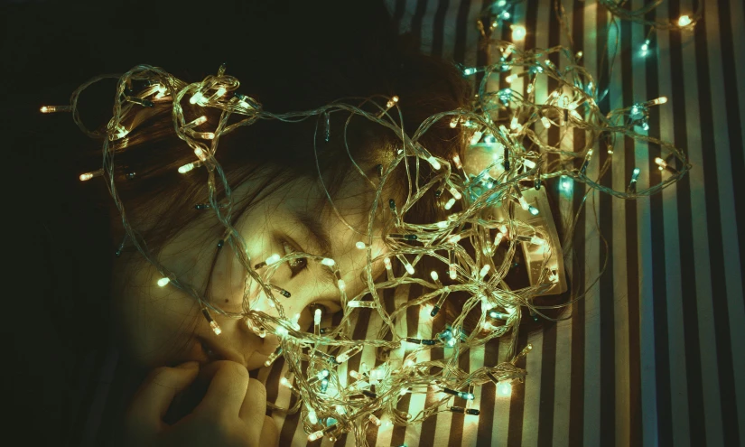 a little girl laying on top of a bed covered in christmas lights, a colorized photo, inspired by Elsa Bleda, tumblr, magical realism, greenish lighting, tangled vines, ilustration, mood scary