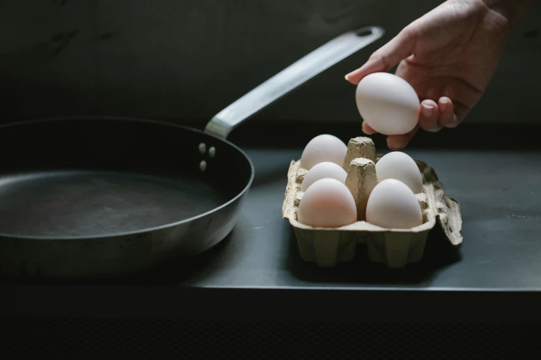 a person putting eggs in a carton into a frying pan, a still life, by Jessie Algie, pexels contest winner, dragon eggs, at the counter, holding an epée, thumbnail