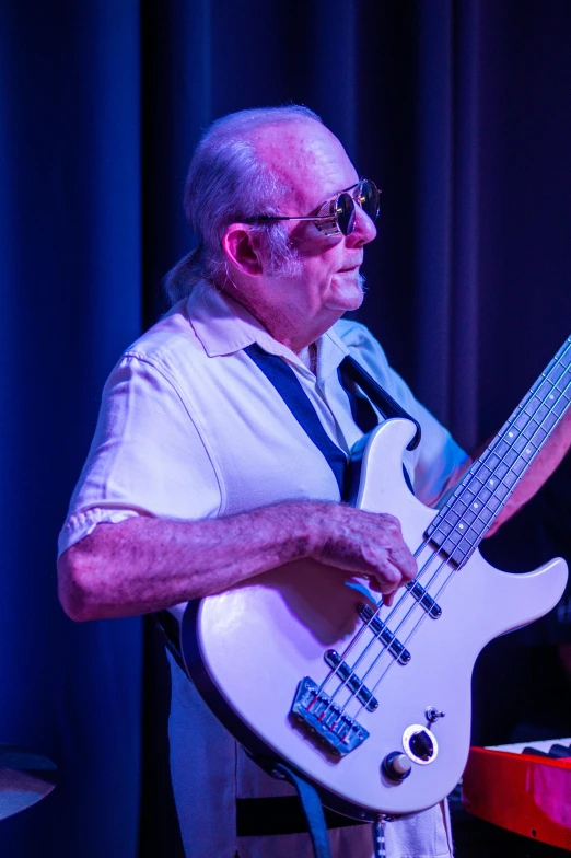 a man that is standing up with a guitar, by Arnie Swekel, double bass, dramatic white and blue lighting, an 80 year old man, lachlan bailey