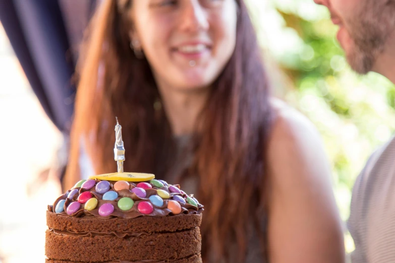 a close up of a person holding a cake with a candle on it, profile image, alana fletcher, multi - coloured, chocolate