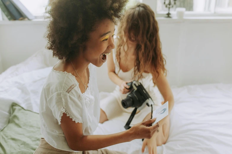 two little girls sitting on a bed playing with a camera, pexels contest winner, happening, woman holding another woman, avatar image, thumbnail, both laughing