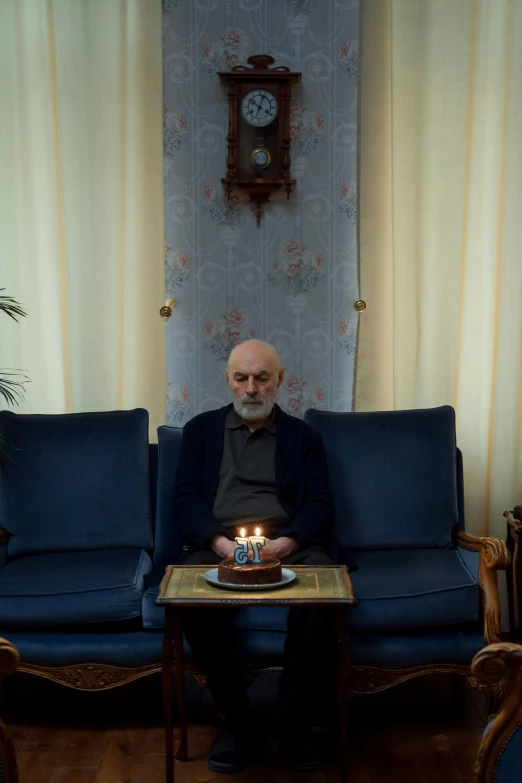 a man sitting on a couch with a cake in front of him, by Elsa Bleda, pexels contest winner, hyperrealism, iran, an oldman, lit with candles, still frame from a movie