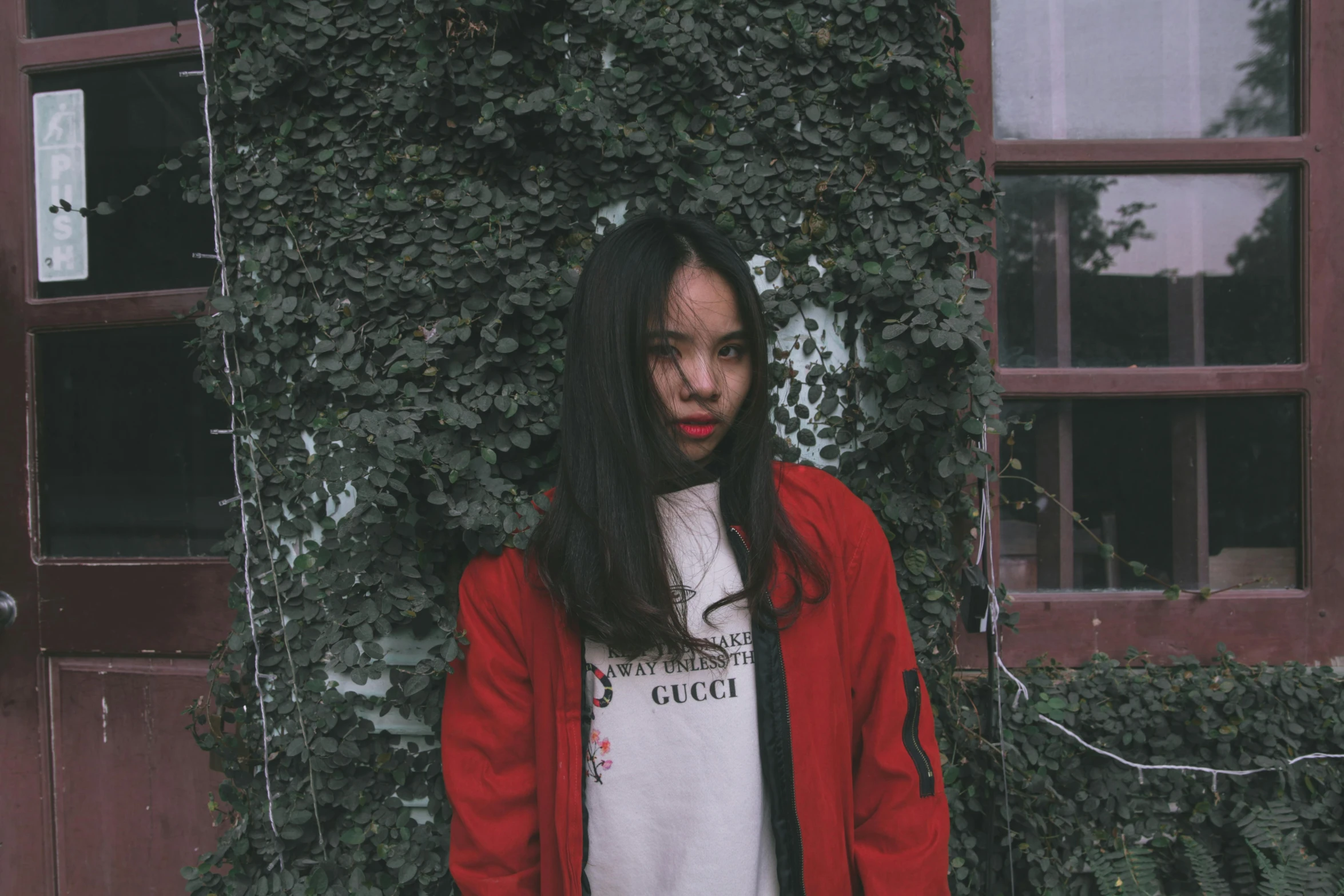 a woman in a red jacket standing in front of a building, pexels contest winner, aestheticism, young cute wan asian face, covered in vines, wearing a t-shirt, guccimaze