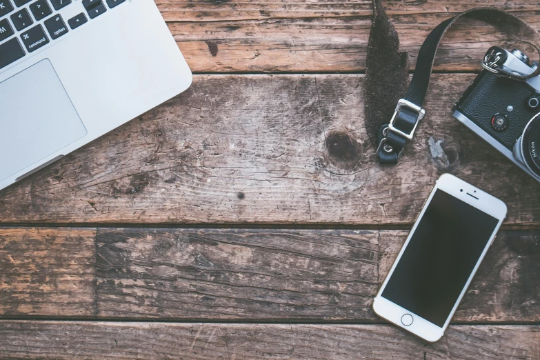 a camera, a cell phone, and a laptop on a wooden table, trending on pexels, background image, 9 9 designs, hunting, vintage photo