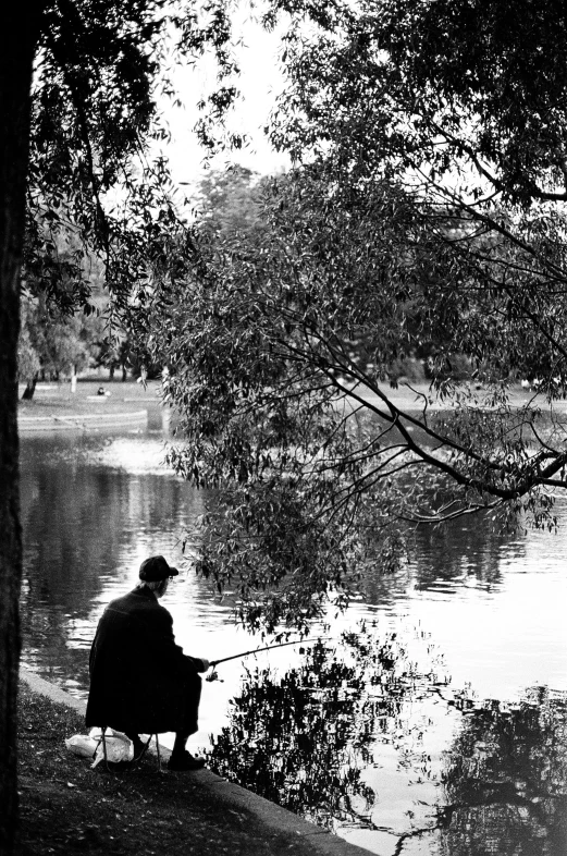 a black and white photo of a man fishing, inspired by Bert Hardy, flickr, city park, sydney park, ffffound, trees reflecting on the lake