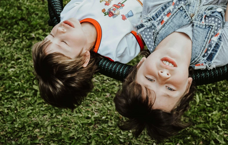 a couple of kids laying on top of a lush green field, pexels contest winner, incoherents, hanging upside down, close up head shot, 15081959 21121991 01012000 4k, swings