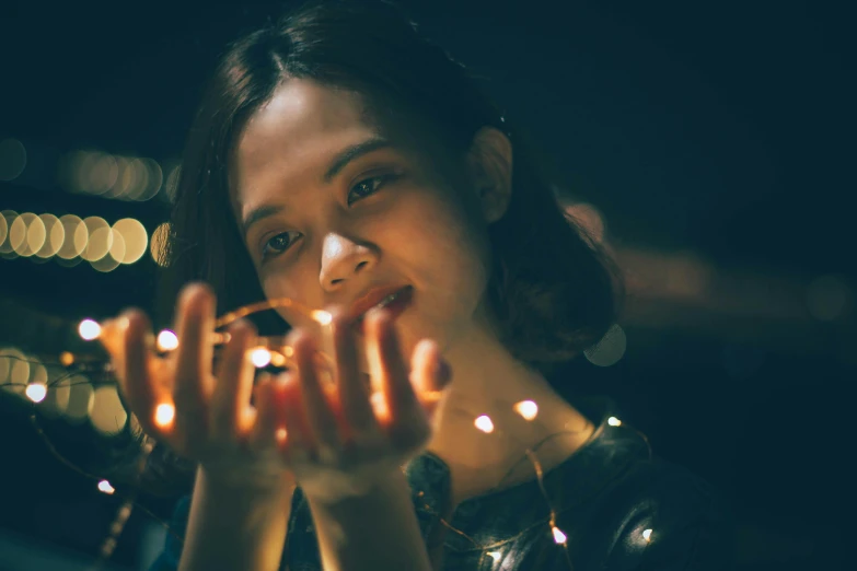 a woman holding a string of lights in her hands, pexels contest winner, visual art, confident looking, hands on face, instagram post, young woman in her 20s