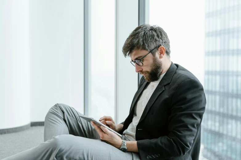 a man sitting on the floor using a tablet computer, trending on pexels, in suit with black glasses, lachlan bailey, thumbnail, looking from shoulder