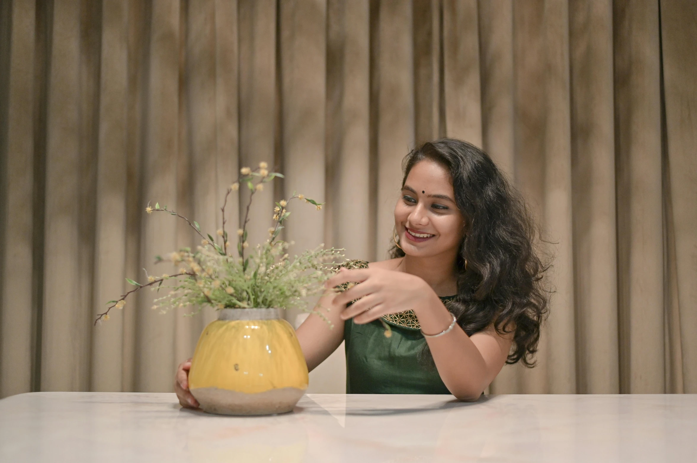 a woman sitting at a table with a vase of flowers, inspired by T. K. Padmini, trending on cg society, hurufiyya, movie still 8 k, cheeky smile, pr shoot, youtube thumbnail