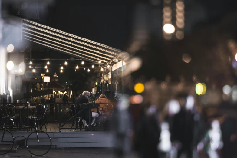 a group of people sitting outside of a restaurant at night, a tilt shift photo, by Nick Fudge, trending on unsplash, canopies, night time render, dark. no text, cafe