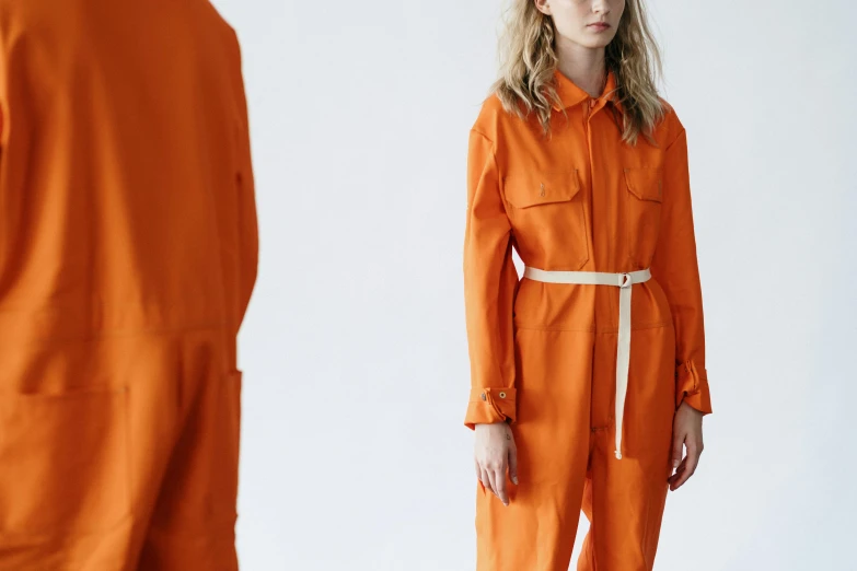 a woman in an orange jumpsuit standing next to a man, inspired by Christo, trending on pexels, renaissance, wearing human air force jumpsuit, zoomed out view, lookbook, full colour