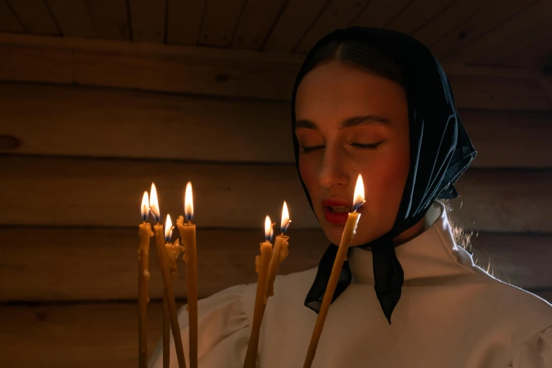 a woman holding a bunch of candles in front of her face, an album cover, inspired by Vasily Perov, pexels contest winner, in orthodox church, russian clothes, profile image, holiday season