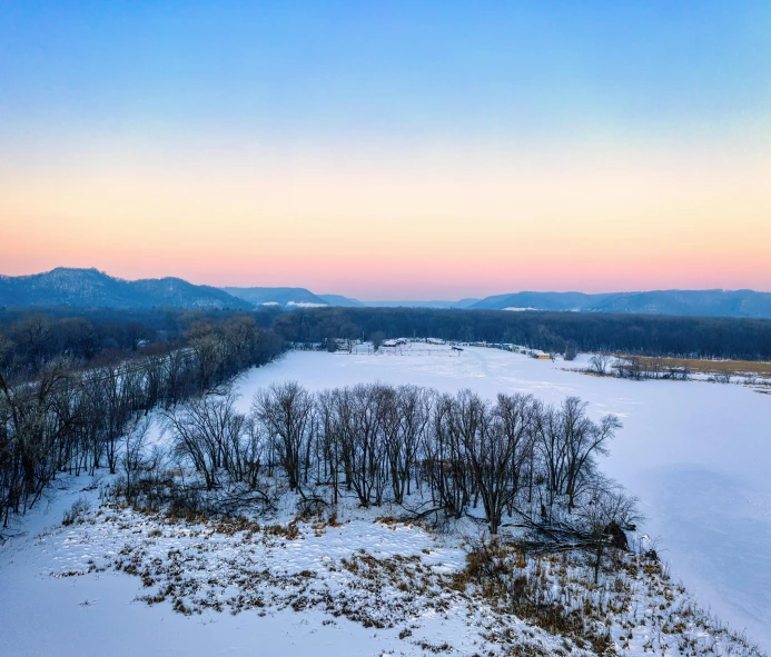 a snow covered field with trees and mountains in the background, a photo, by Andrew Stevovich, pexels contest winner, hudson river school, golden and blue hour, wide high angle view, minn, ai weiwei and gregory crewdson