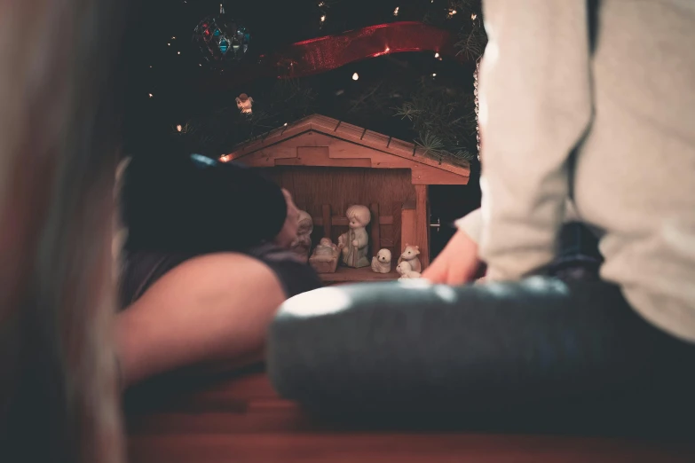 a person sitting in front of a christmas tree, by Daniel Lieske, pexels contest winner, art toys on feet, jesus wasted at a party, in a cabin, he holds her while she sleeps