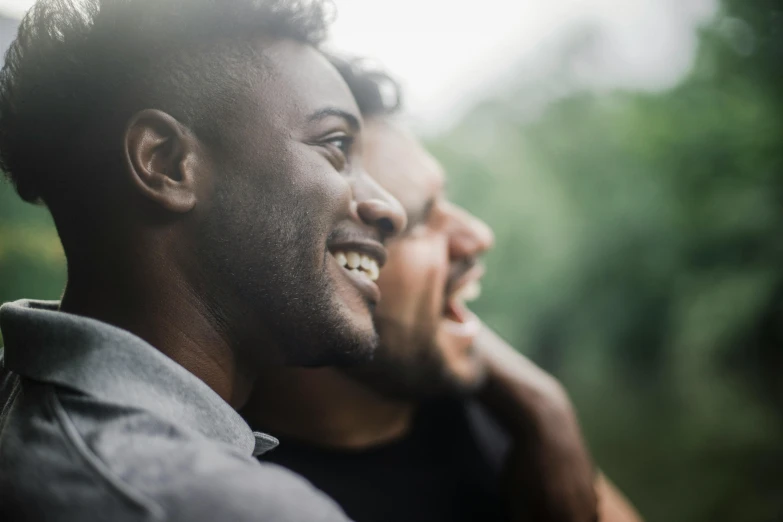 a couple of men standing next to each other, trending on unsplash, brown skin man with a giant grin, looking outside, background image, a close up shot