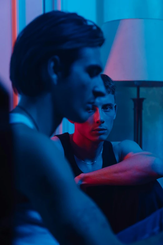 a couple of people sitting on top of a couch, inspired by Nan Goldin, trending on pexels, bauhaus, blue and red lights, chiseled jawline, teenage boy, looking serious