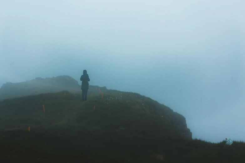 a person standing on top of a hill on a foggy day, a picture, looking for clues, unsplash photography, distant hooded figures, slightly pixelated