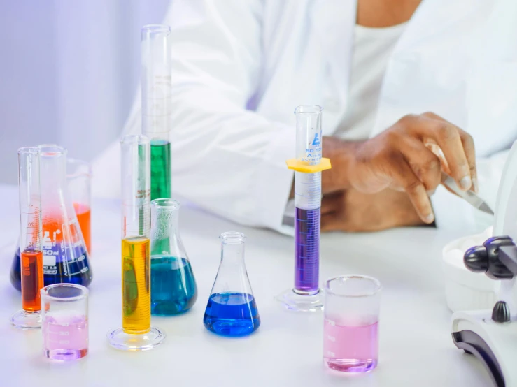 a close up of a person in a lab coat, trending on pexels, process art, beakers of colored liquid, on a white table, medical labels, purple