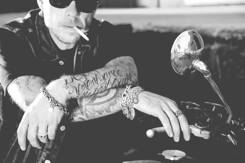 a man sitting on a motorcycle smoking a cigarette, a black and white photo, inspired by David Begbie, wearing two silver bracelets!, linkin park, wearing jewelry, tatoo