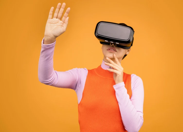 a woman wearing a virtual reality headset on an orange background, trending on pexels, wave a hand at the camera, avatar image