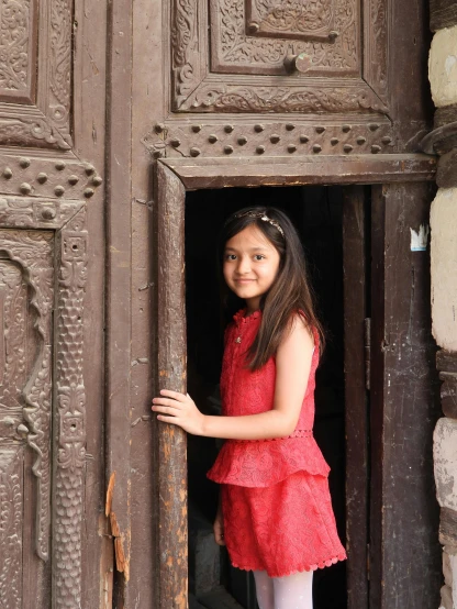 a little girl that is standing in a door, a picture, pexels contest winner, hurufiyya, beautiful young himalayan woman, brown:-2, low quality photo, wearing dress