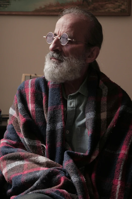 a man sitting on top of a couch covered in a blanket, inspired by Alasdair Gray, trending on reddit, gray beard, profile image, standing in a dimly lit room, wearing a flannel shirt