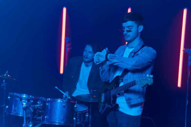 a group of men standing next to each other on a stage, an album cover, by Robbie Trevino, pexels, blue light, playing drums, charli bowater, looking left