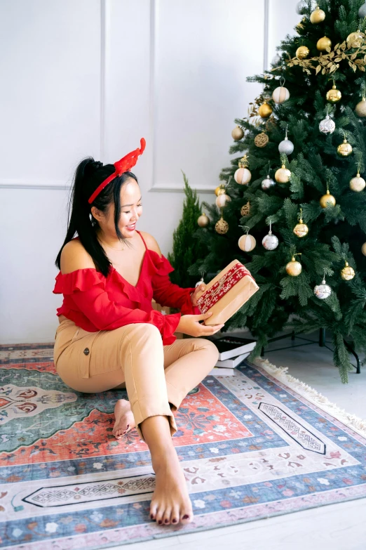 a woman sitting in front of a christmas tree reading a book, a cartoon, pexels contest winner, hurufiyya, vietnamese woman, red shirt brown pants, holding gift, gif