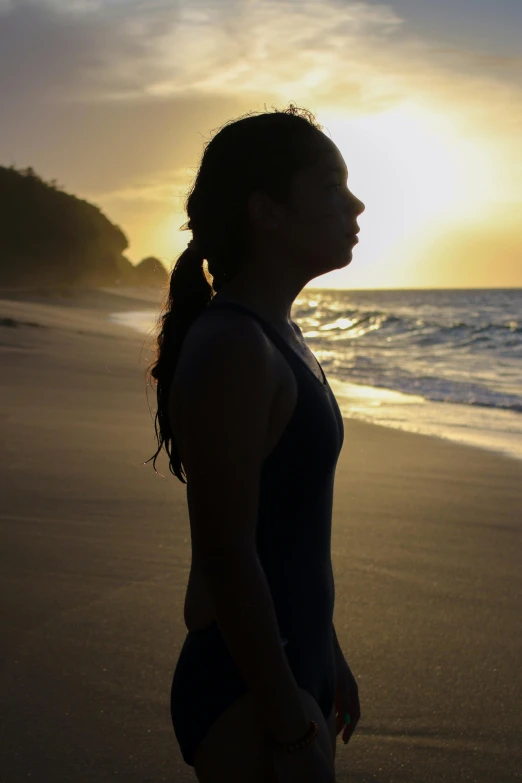 a woman standing on top of a beach next to the ocean, backlit face, profile image, standing athletic pose, at peace