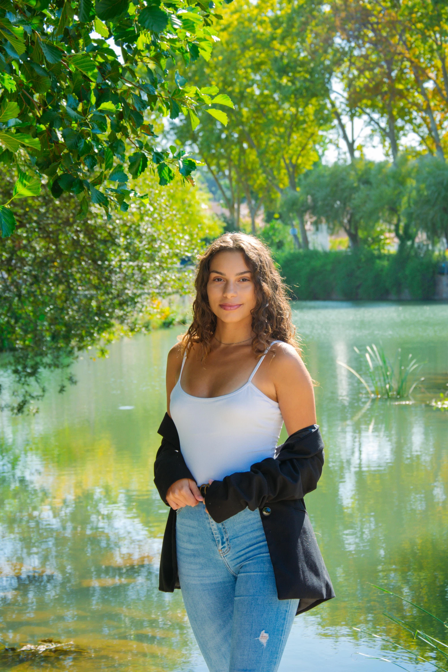 a woman standing next to a body of water, portrait demi rose, seville, in a park and next to a lake, avatar image