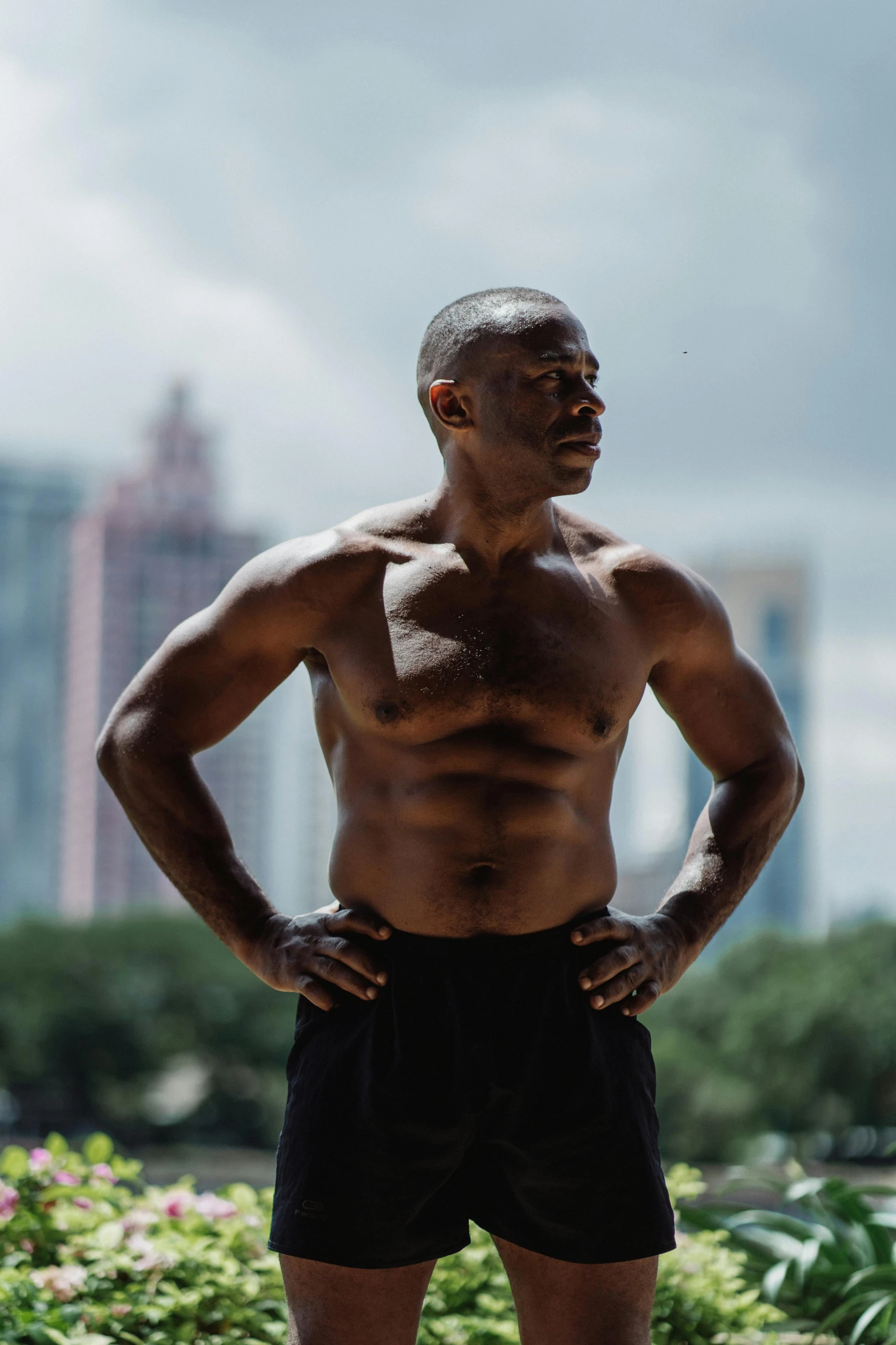 a man standing with his hands on his hips, by Austin English, wrinkles and muscles, black man, with a city in the background, working out