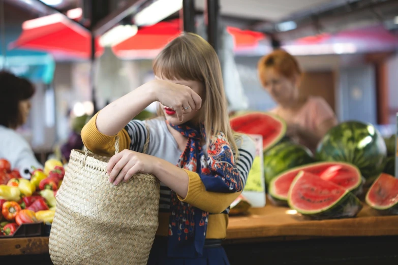 a woman holding a straw bag in front of a fruit stand, by Julia Pishtar, pexels contest winner, exasperated expression, watermelon, teenage girl, obscured underexposed view